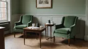 Deux fauteuils verts vides de part et d'autre d'une table en bois où attendent des feuilles imprimées, un stylo et deux tasses