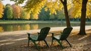 Deux chaises de jardin en métal vert face à un étang de parc urbain, lumière rasante de fin d'après-midi en automne